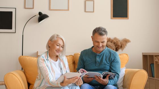 Un couple de sexagénaires assis dans un canapé, en train de lire une revue et de discuter.
